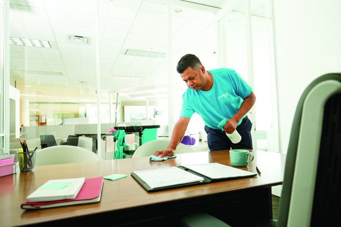 KPC staff in blue uniform cleaning office desk